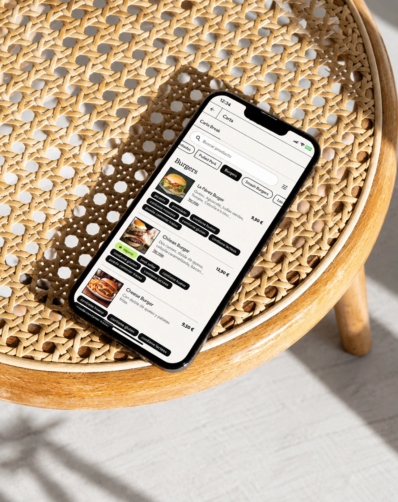 La app de PilloSitio en un móvil sobre un taburete de rejilla