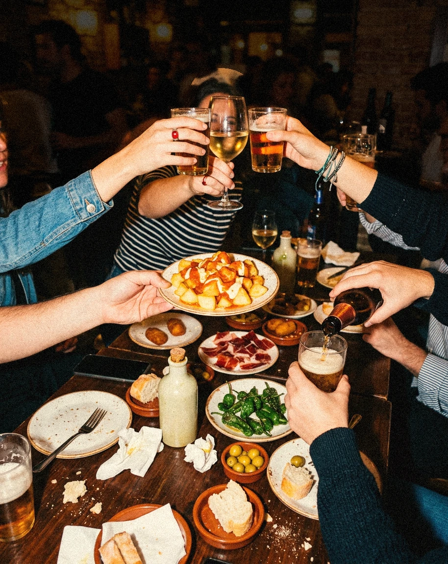 Amigos brindando en un bar de tapas, con cañas, bravas y jamón en la mesa