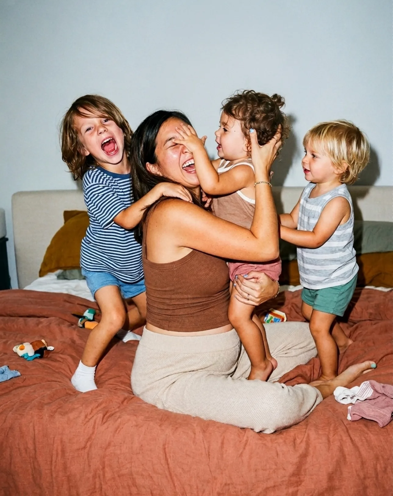 A mother playing with her three children on the bed